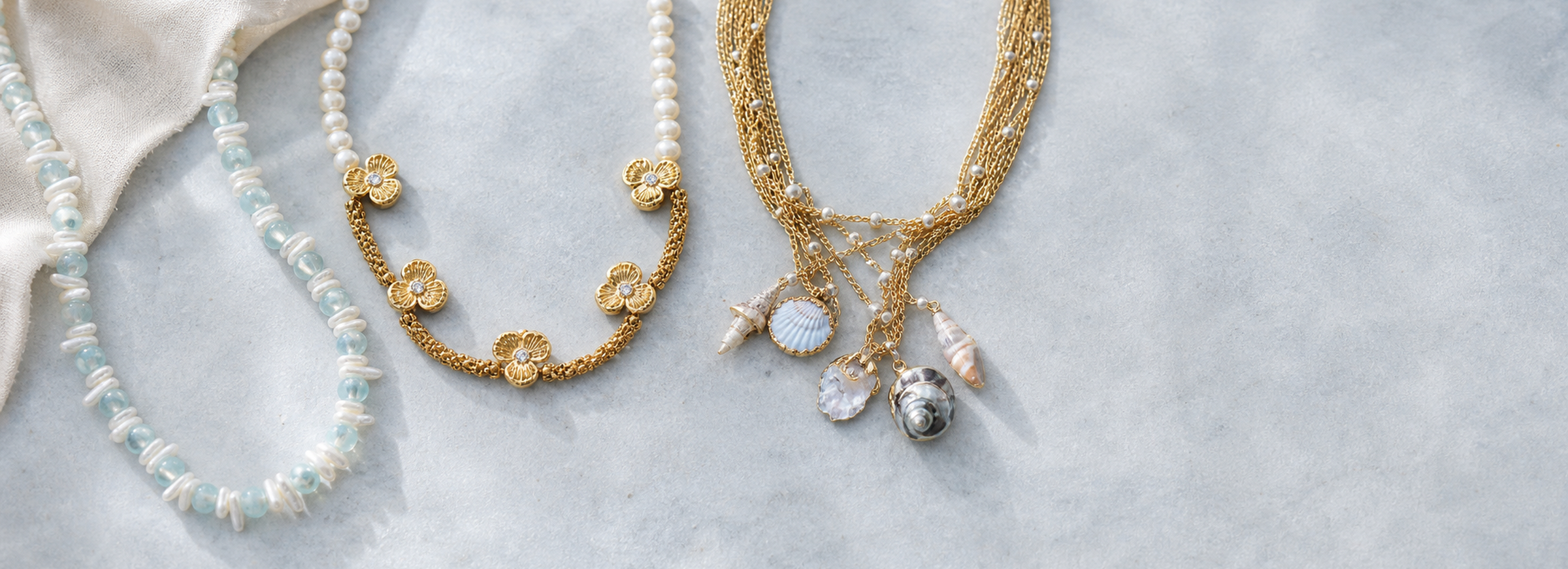 Pearl necklace with shell and initial charms on a cool textured surface